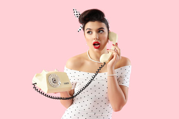 Young pin-up woman talking by telephone on pink background