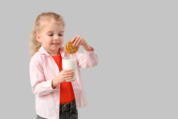 Cute little girl with glass of milk and cookie on light background