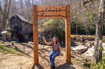 Woman on the Almost Heaven Swing in Front of the Glade Creek Grist Mill and Waterfall in West Virgina During a Sunny Spring Day