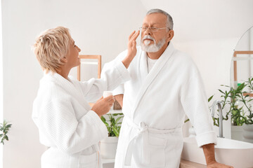 Mature couple applying facial cream in bathroom