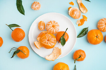 Plate with tasty tangerines and leaves on blue background