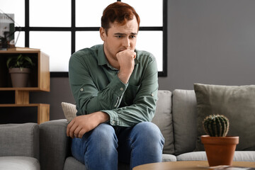 Young man with hemorrhoids sitting on sofa at home