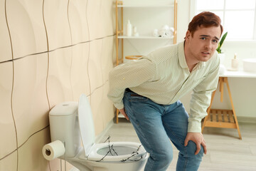 Young man with hemorrhoids and barbed toilet bowl in restroom