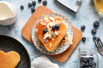 Plate with tasty pancakes in shape of heart, blueberry and nuts on blue background. Valentine's Day celebration