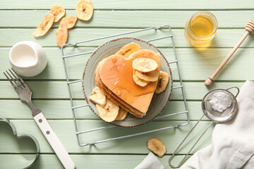 Plate with tasty pancakes in shape of heart, dried banana and honey on green wooden background. Valentine's Day celebration