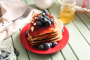 Plate with tasty pancakes in shape of heart, blueberry and jam on green wooden background, closeup. Valentine's Day celebration
