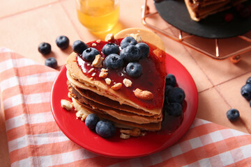 Plate with tasty pancakes in shape of heart, blueberry and nuts on beige tile background, closeup. Valentine's Day celebration