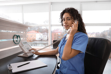 Female African-American medical intern talking by telephone at reception in clinic - obrazy, fototapety, plakaty