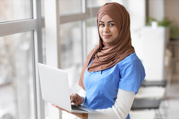 Female Muslim medical intern with laptop in clinic