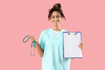Female African-American medical intern with stethoscope and clipboard on pink background