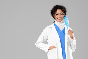 Female African-American medical intern with mask on light background