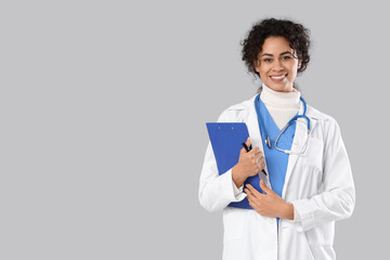 Female African-American medical intern with clipboard on light background