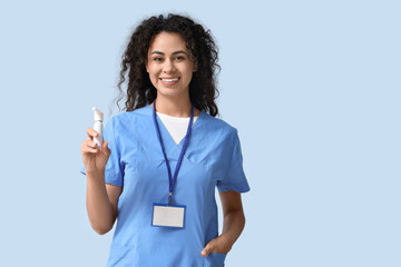 Female African-American medical intern with spray bottle on blue background
