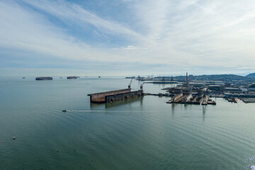 Fototapeta premium aerial shot of the San Francisco Bay with cargo ships on the rippling ocean water, cranes, buildings, blue sky and clouds at sunset in San Francisco California USA