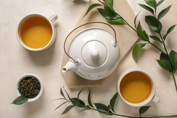 Teapot with cups, bowl of dry tea and leaves on white grunge background