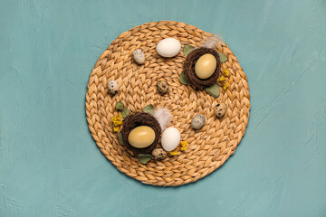Straw mat with Easter eggs, flowers and leaves on blue background