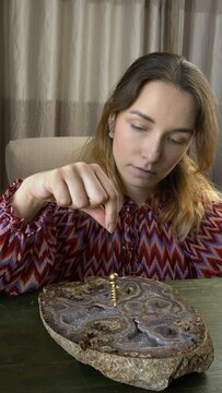 A young woman holding a moving pendulum over a large agate slice on a green wooden table.