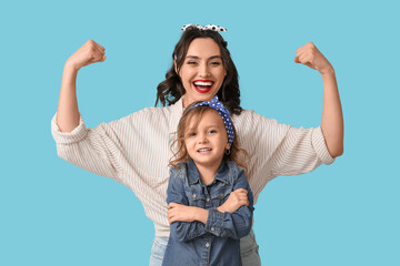 Beautiful pin-up woman showing muscles and her daughter on blue background