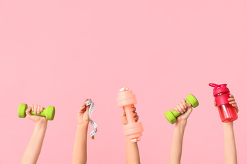 Female hands with dumbbells, measuring tape and bottle of water on pink background
