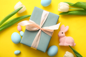 Easter eggs, tulip flowers with gift box and bunny on yellow background
