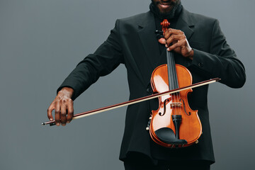 Elegant African American man in tuxedo playing violin against gray background with grace and talent