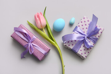 Easter eggs with gift boxes and tulip flower on grey background