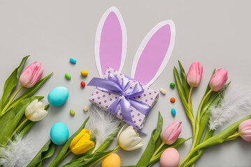 Easter eggs with gift box, tulip flowers and paper bunny ears on grey background