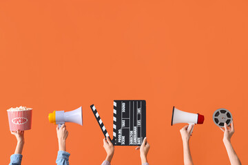 Many hands with bucket of popcorn, movie clapper and megaphones on orange background