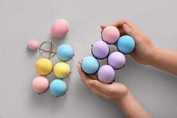 Female hands and holders with painted Easter eggs on grey background