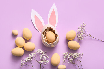 Painted Easter eggs with gypsophila flowers and paper bunny ears on purple background