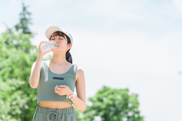 公園で水・ミネラルウォーターを飲む女性（水分補給・運動・ワークアウト・ランニング・ウォーキング）
