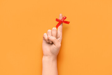 Female hand with red bow on index finger against orange background. Reminder concept