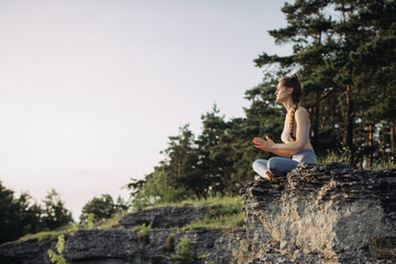 Naklejka na ściany i meble A young woman practices yoga and meditates in the mountains at sunset. Peace and unity with nature.