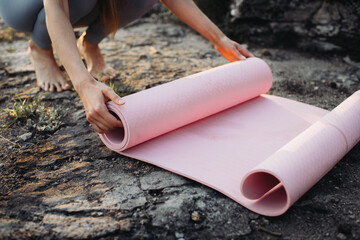 A young woman in fitness clothes rolls up her yoga mat after a workout in a beautiful mountain location.
