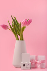 Vase with beautiful tulips, cube calendar and gift box on pink background. International Women's Day