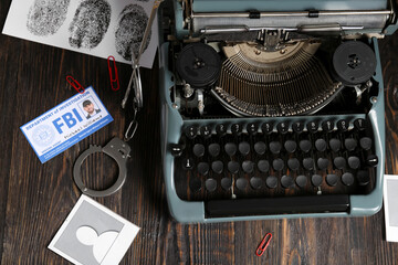 Retro typewriter, handcuffs, document of FBI agent and fingerprints on wooden table
