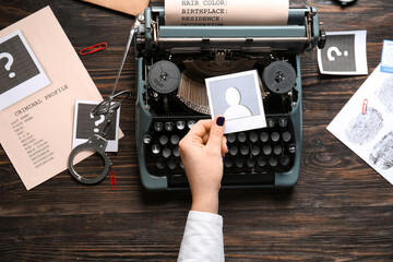 Female hand with vintage typewriter, handcuffs and criminal files on wooden background