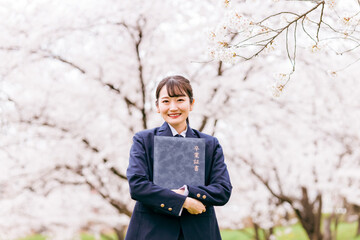 満開の桜の下で卒業証書を持つ高校生・女子高生（卒業生・卒業式・卒業）
