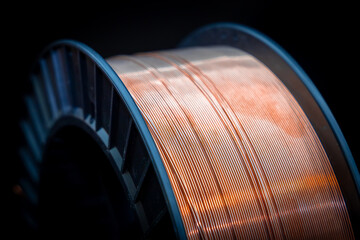 Black plastic spool with shiny copper wire. Shiny copper wire wound on a reel, dark background,...