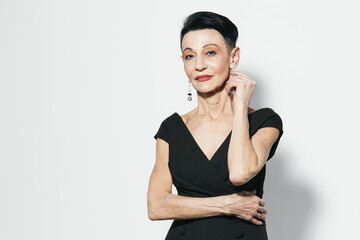 Elderly woman in elegant black dress confidently posing with hands on hips for the camera portrait