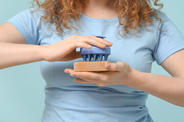 Young woman with hair scalp massager and shampoo bar on blue background