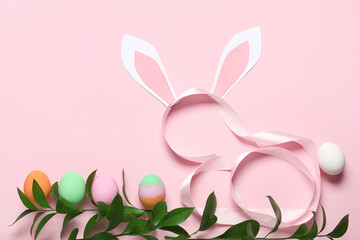 Composition with painted Easter eggs, green branch, ribbon and paper bunny ears on pink background
