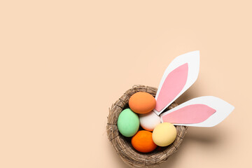 Wicker nest with painted Easter eggs and paper bunny eggs on beige background