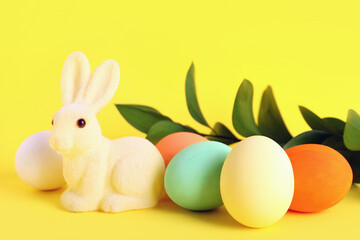 Painted Easter eggs, green branch and bunny on yellow background, closeup