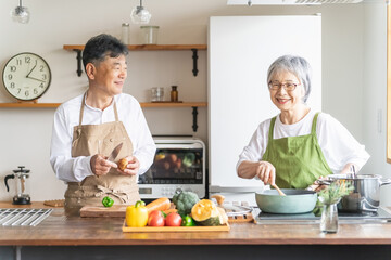 家のキッチンで一緒に料理・家事を楽しむ高齢者夫婦・シニアカップル
