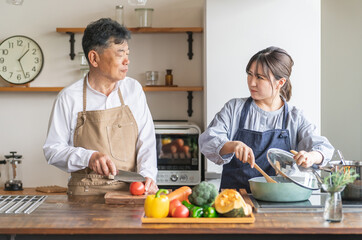 家のキッチンで料理に文句をいうアジア人高齢者男性と若い女性（家政婦・家事代行）
