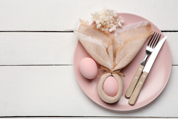 Beautiful table setting with Easter eggs, napkin, flowers and cutlery on white wooden background