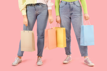 Beautiful happy women in stylish jeans with shopping bags on pink background