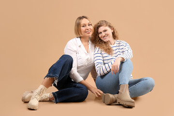 Obraz na płótnie Canvas Beautiful happy women in stylish jeans sitting on beige background