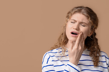 Beautiful young woman suffering from toothache on brown background